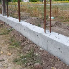 Solidna podmurówka pod siatkę, z wystającymi prętami zbrojeniowymi, gotowa na dalsze prace budowlane.