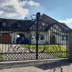 Eleganckie, dwuskrzydłowe bramy kute chronią posesję z białym domem i niebieskim samochodem.