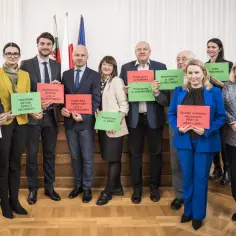 Grupa osób w garniturach i strojach biznesowych trzyma tabliczki z nazwami projektów inwestycyjnych w Lublinie.