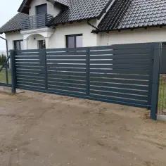 Nowoczesne rodzaje bram wjazdowych: przesuwna, ciemnoszara, z poziomymi szczelinami, idealnie komponuje się z domem.