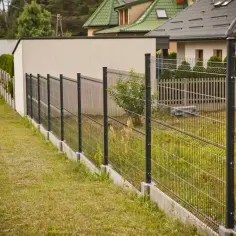 Ogrodzenie panelowe na pochyłym terenie, z betonowym podmurówką, tworzy estetyczną barierę.
