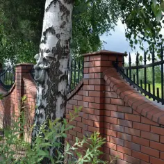 Nowoczesne ogrodzenie z cegły z ozdobnym kutym elementem na pniu brzozy.