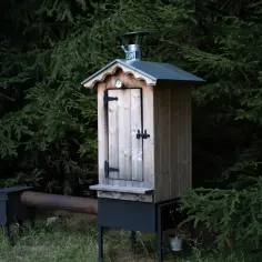 Drewniana wędzarnia z metalowym paleniskiem i rurą, gotowa do wędzenia. Idealna do ogrodu, gdy chcesz wiedzieć, jak zrobić palenisko do wędzarni.