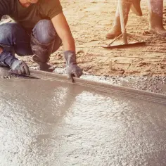 Pracownik wyrównuje świeżą wylewkę betonową za pomocą łaty. Dowiedz się, jak zrobić wylewkę betonową.