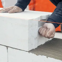 Ręce budowlańca podczas murowania ścianek działowych z bloczków betonowych. Widać zaprawę i sznur murarski.