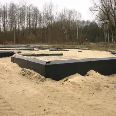 Fundamenty domu w piasku, zabezpieczone czarną folią. Trwa hydroizolacja ścian fundamentowych.