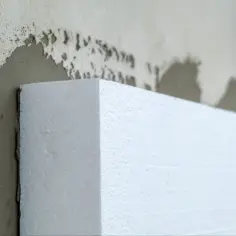 Fragment białego styropianu przyłożony do ściany z zaprawą. To materiał izolacyjny, nie styrobeton.