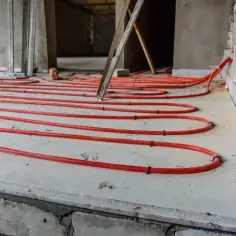 Czerwone rury ogrzewania podłogowego ułożone na styropianie. Minimalna grubość styropianu pod ogrzewanie podłogowe jest kluczowa dla efektywności.