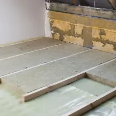 Ocieplenie stropu betonowego styropianem w trakcie prac. Płyty izolacyjne ułożone na folii, podparte drewnianymi legarami.