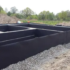 Fundament domu w trakcie budowy, z czarną membraną kubełkową i żwirem. To kluczowy etap, jak ocieplić fundament, by zapewnić trwałość i komfort.