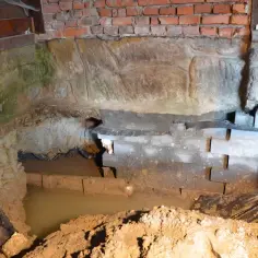 Prace przy hydroizolacji fundamentów od wewnątrz. Widoczny wykop, wilgoć i elementy konstrukcyjne.