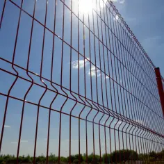 Czerwone panele ogrodzeniowe, gotowe do montażu, lśnią w słońcu na tle błękitnego nieba.