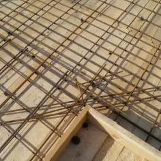 Siatka zbrojenia górnego stropu na drewnianym deskowaniu. Stalowe pręty tworzą regularną kratownicę, gotową na zalanie betonem.
