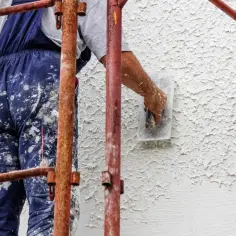 Robotnik w brudnych spodniach nakłada tynk baranek na elewację.