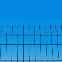Siatka ogrodzeniowa na tle błękitnego nieba. Trwają prace nad ustawianiem słupków ogrodzeniowych, tworząc solidną barierę.