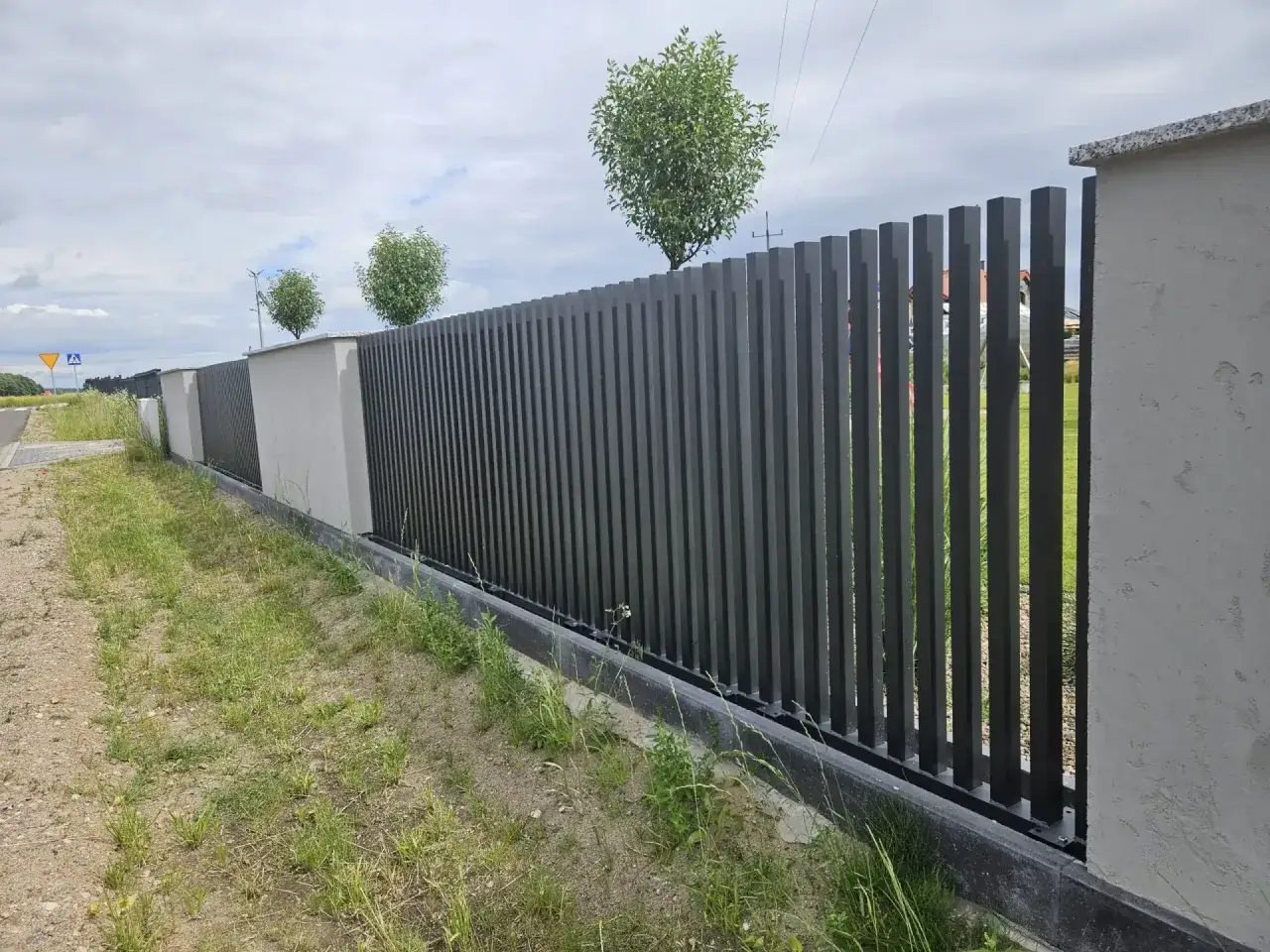 Nowoczesne ogrodzenie z pionowych słupków, idealne rozwiązanie jak ustawić słupki ogrodzeniowe na nierównym terenie.