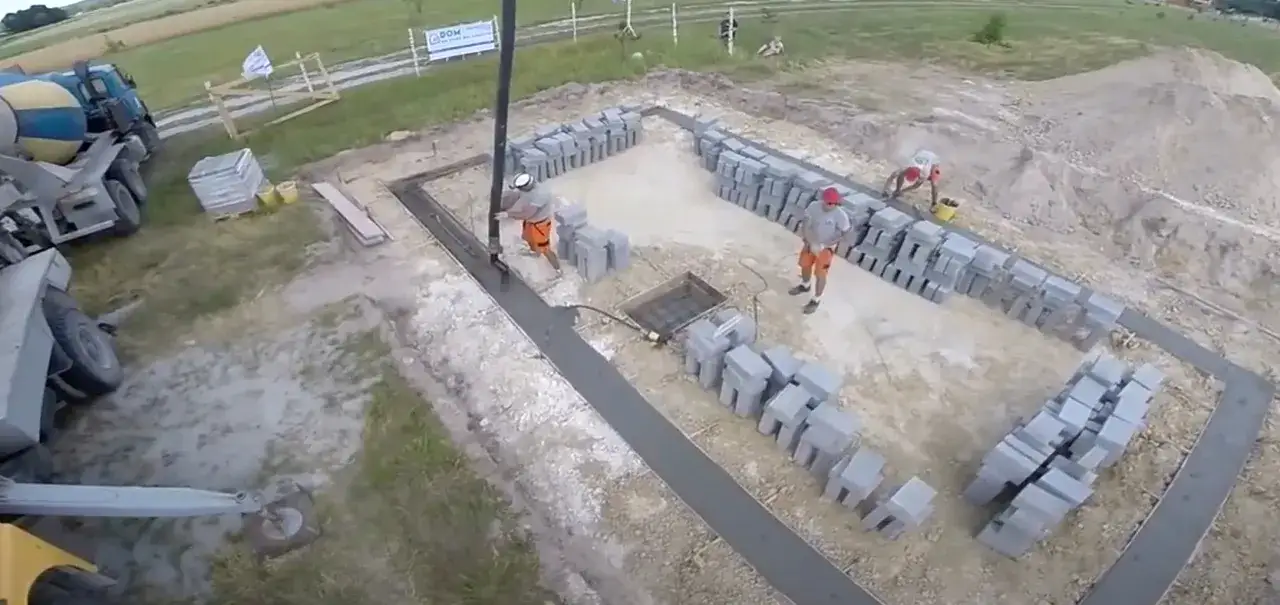 Budowa domu: ławy fundamentowe krok po kroku. Beton wylewany do wykopu, pracownicy układają bloczki.