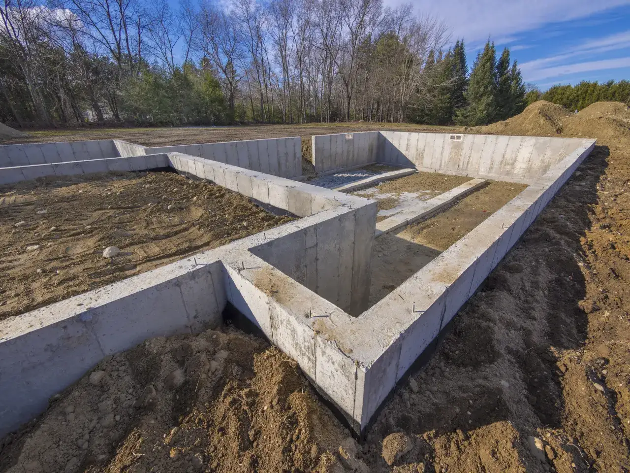 Betonowe ławy fundamentowe krok po kroku. Fundament domu w budowie, otoczony ziemią i drzewami.