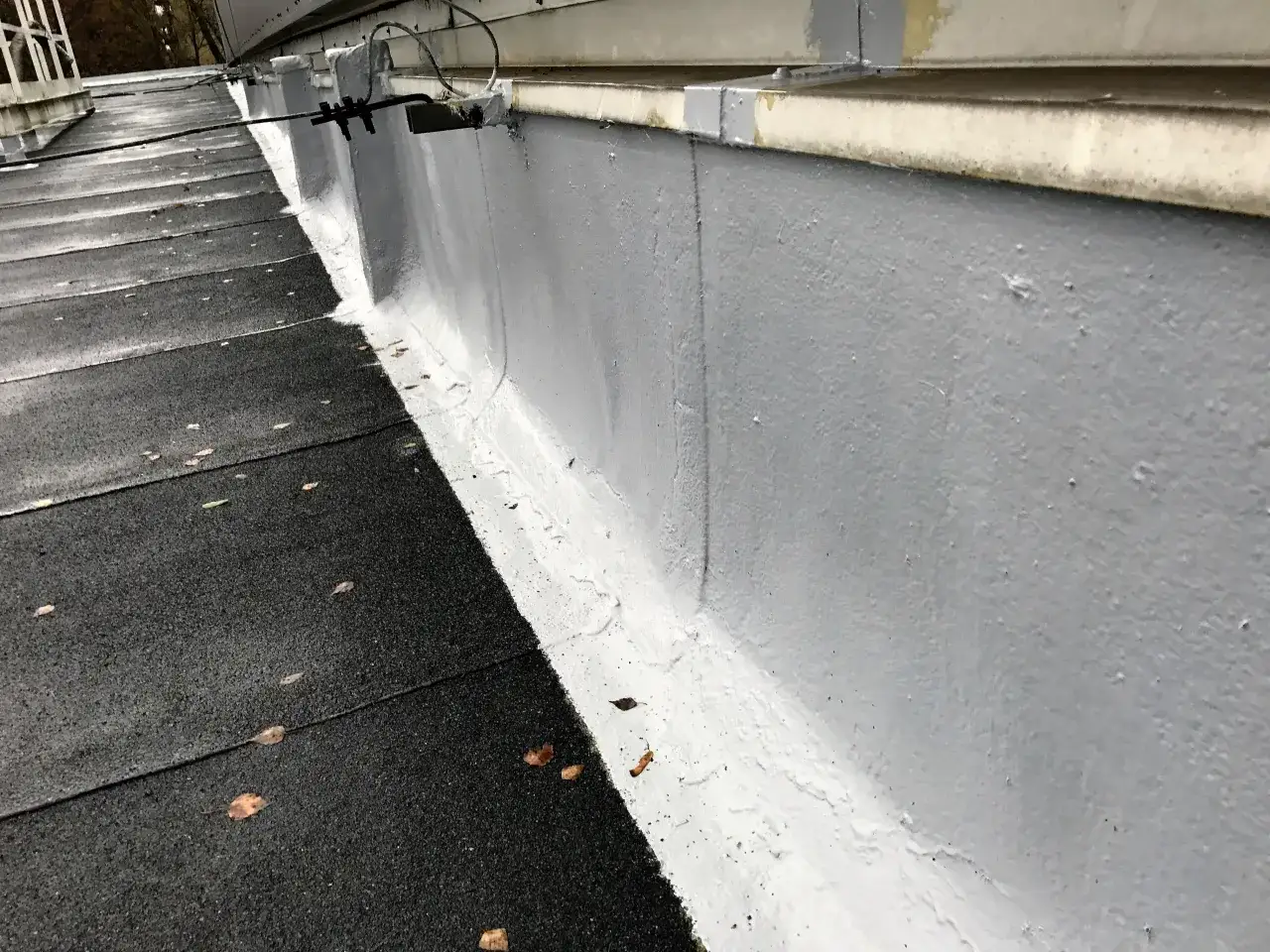 Szara ściana i czarny dach pokryty papą, zabezpieczone nową hydroizolacją.