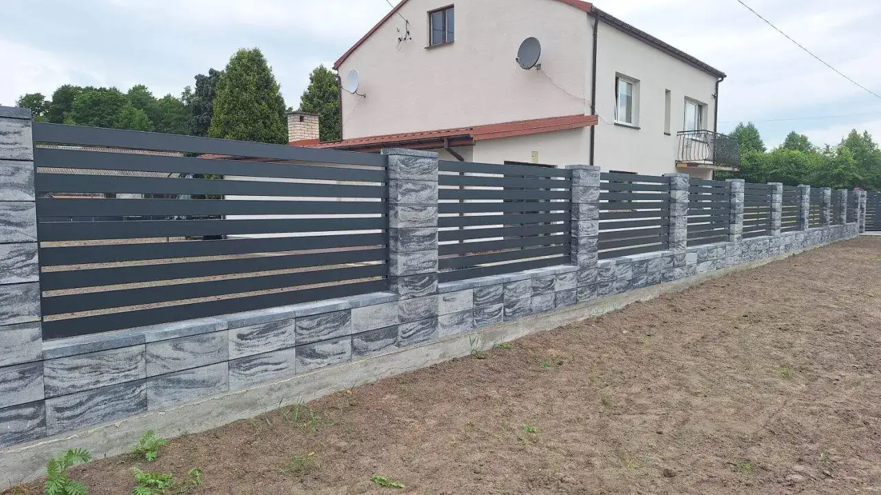 Nowoczesne ogrodzenie z betonu lanego, z szarymi elementami imitującymi kamień i ciemnymi, poziomymi listwami.