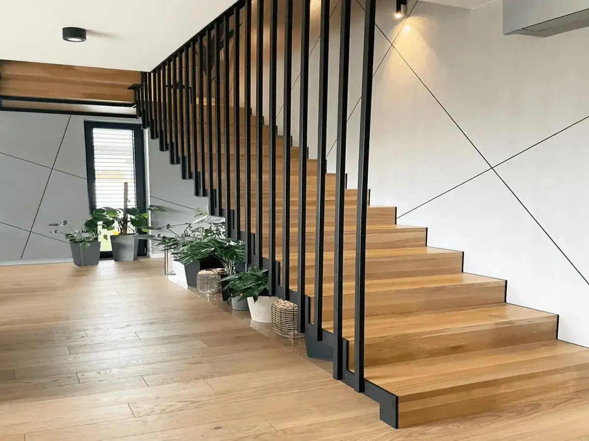 Drewniane schody z czarną balustradą i roślinami w doniczkach w nowoczesnym wnętrzu.