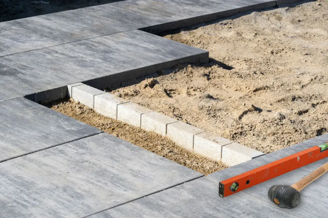 Układanie płyt tarasowych na suchym betonie. Widać narzędzia: poziomicę i gumowy młotek.