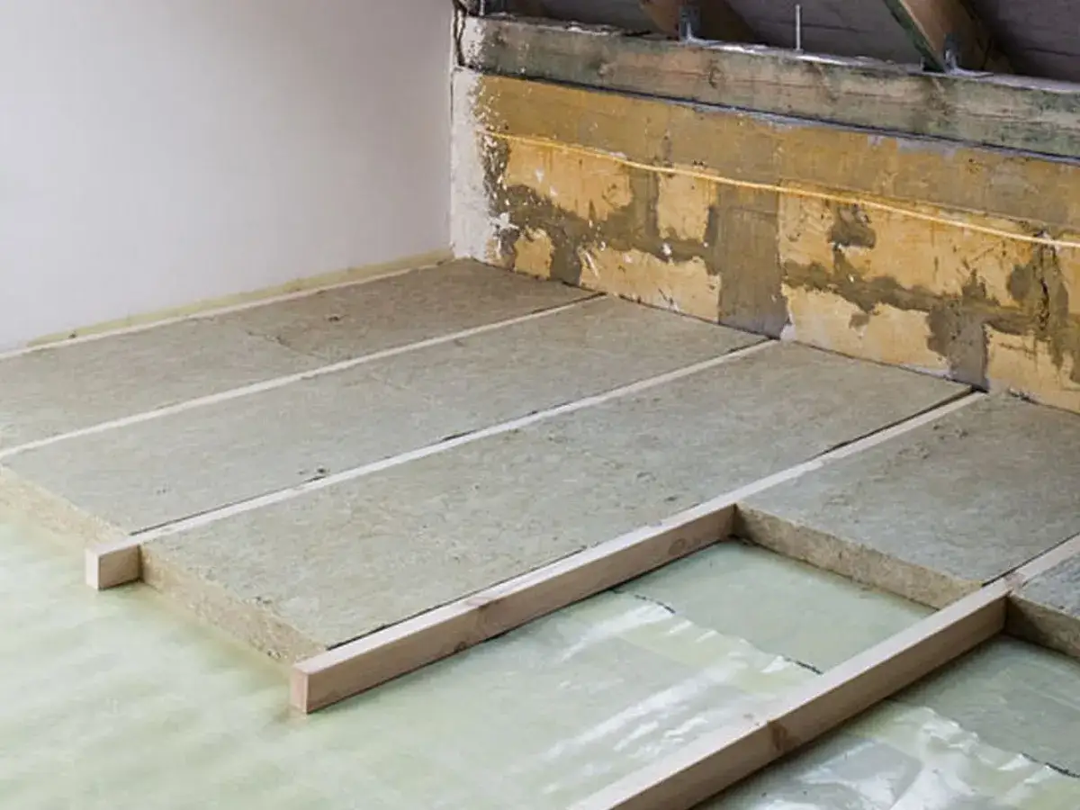 Ocieplenie stropu betonowego styropianem w trakcie prac. Płyty izolacyjne ułożone na folii, podparte drewnianymi legarami.