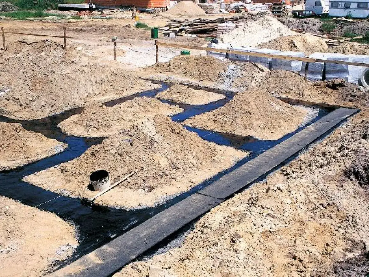 Budowa ław fundamentowych krok po kroku: wykopane rowy wypełnione wodą, otoczone usypaną ziemią.
