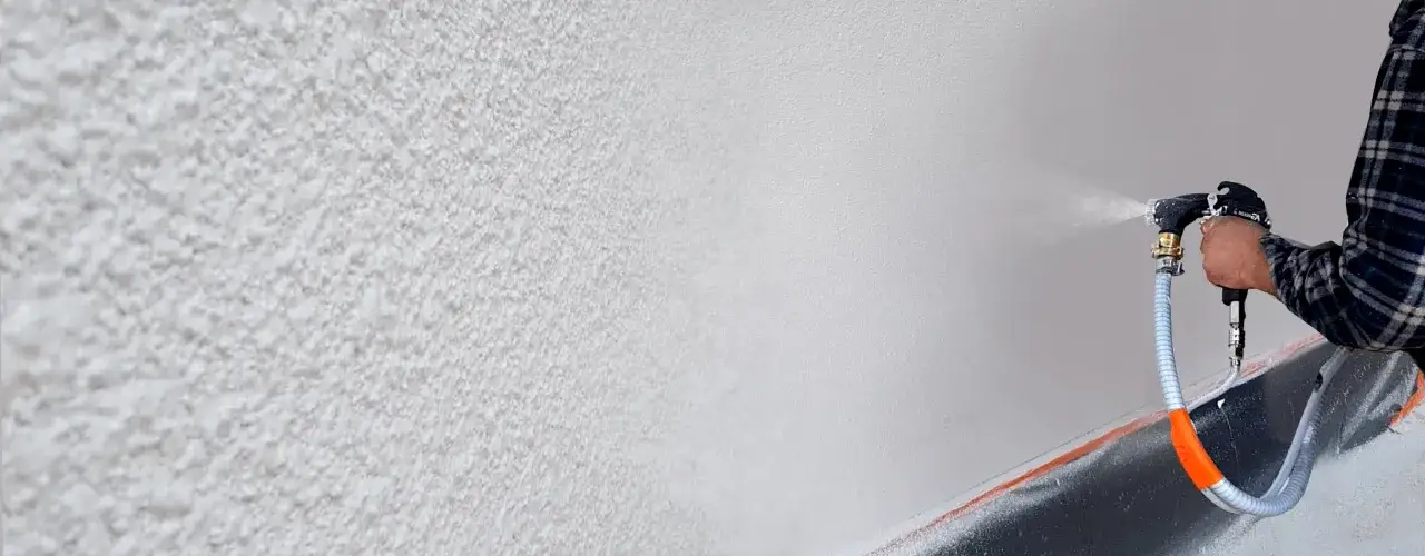 Osoba w kratę nakłada tynk strukturalny na ścianę za pomocą agregatu. Tak zrobisz baranka na ścianie.