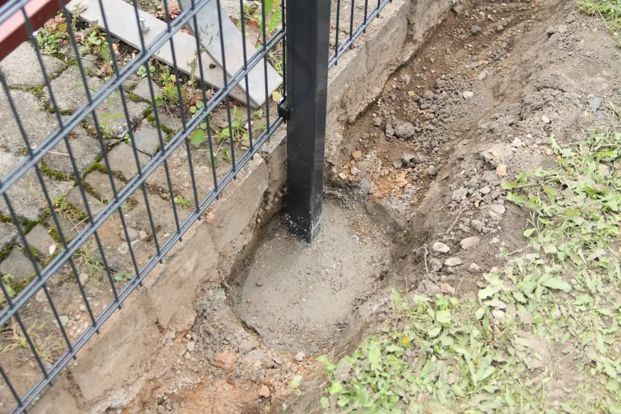 Słupek ogrodzeniowy osadzony w betonie, pokazujący jak ustawić słupki ogrodzeniowe na nierównym terenie.