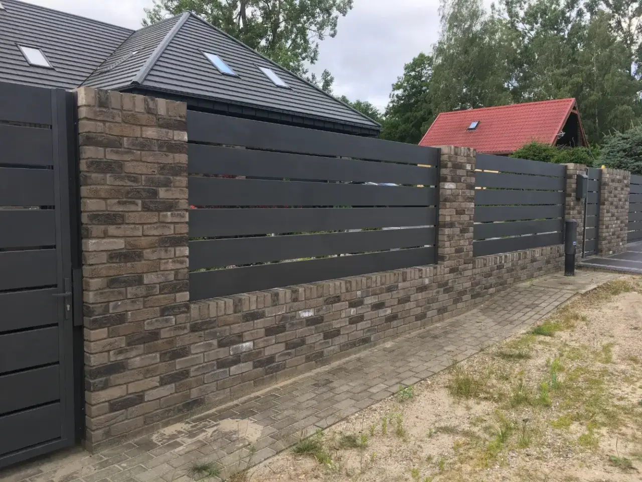 Nowoczesne ogrodzenie z cegły i ciemnoszarych paneli, z bramą wjazdową.