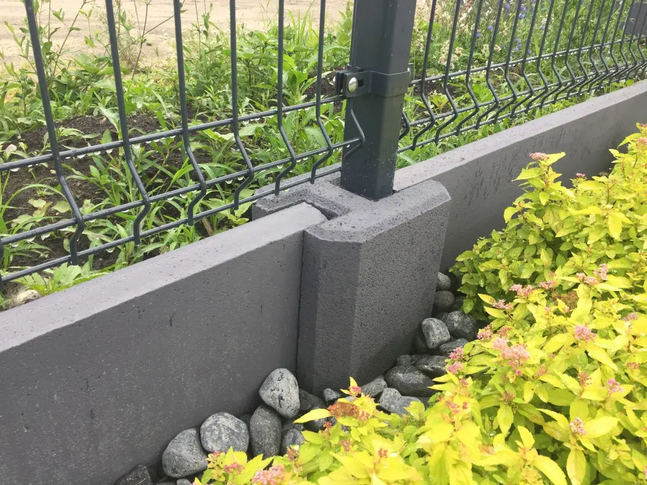Solidna podmurówka pod plot, wykonana z betonowych bloczków, stanowi stabilne oparcie dla metalowej siatki.