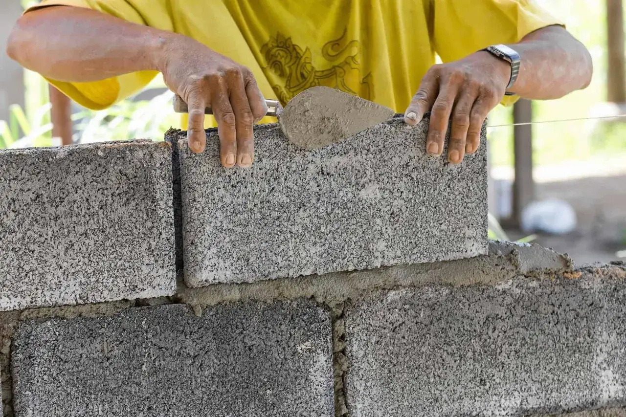 Budowniczy układa bloczek betonowy na zaprawie, tworząc solidny mur.