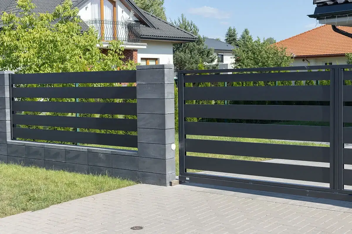 Nowoczesny materiał na ogrodzenie: ciemnoszara, pozioma przęsła z betonowymi słupkami i cokołem. Brama wjazdowa.