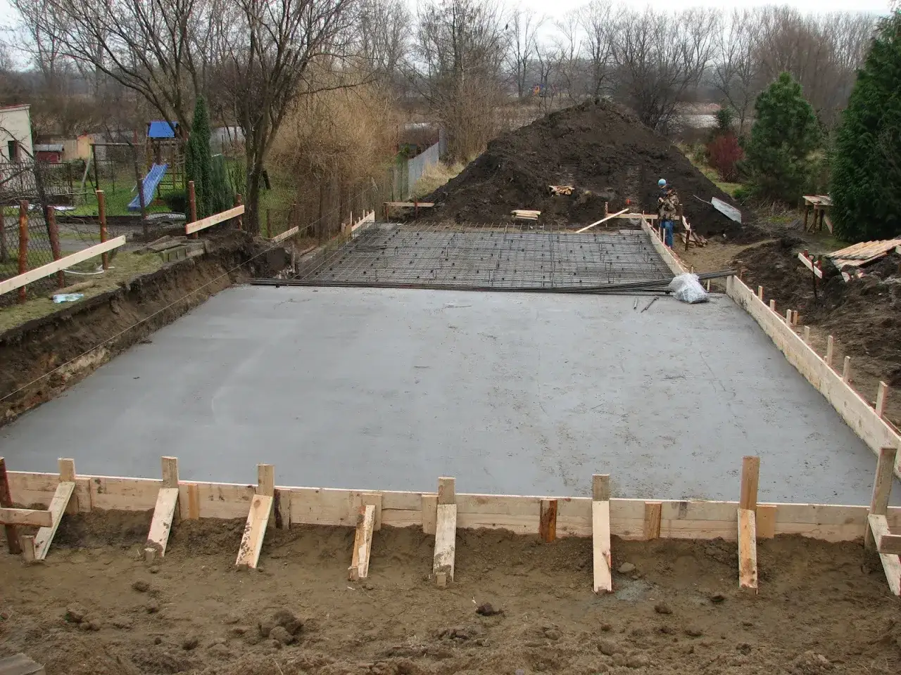 Budowa ław fundamentowych krok po kroku: wylana płyta betonowa, zbrojenie i szalunki.