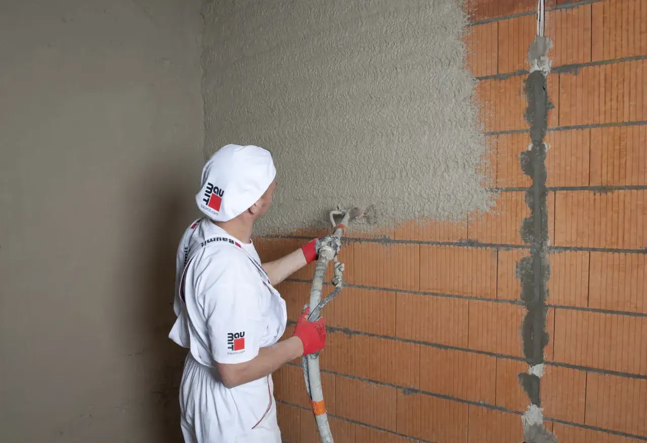 Pracownik nakłada tynk cementowo-wapienny na ścianę z pustaków ceramicznych. Właściwe proporcje składników zapewniają trwałość i estetykę.