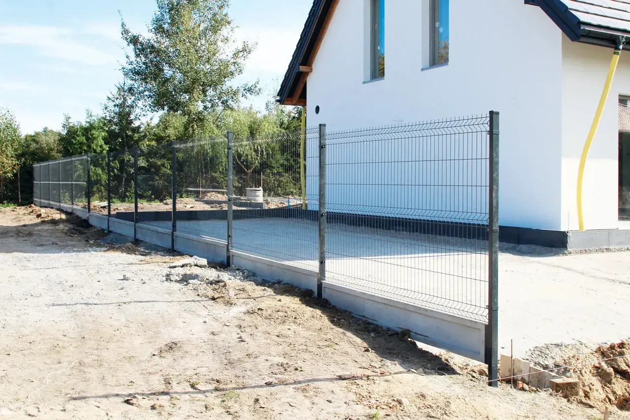 Nowy płot z siatki ogrodzeniowej otacza plac budowy wokół białego domu.