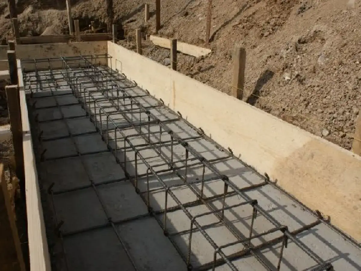 Zbrojenie ław fundamentowych krok po kroku. Betonowe podłoże i drewniane szalunki tworzą podstawę dla stalowej konstrukcji.