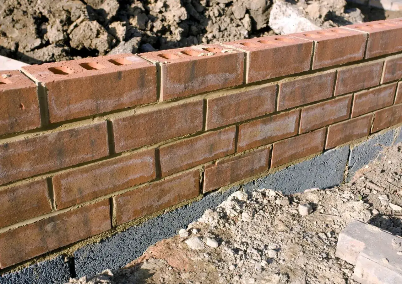 Ceglana ściana ogrodzenia z widoczną warstwą bloczków betonowych, stanowiącą alternatywę dla tradycyjnej podmurówki.
