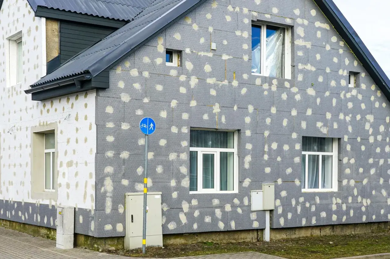 Dom w trakcie ocieplania styropianem. Szare płyty z widocznymi punktami kleju, przygotowane pod tynk.