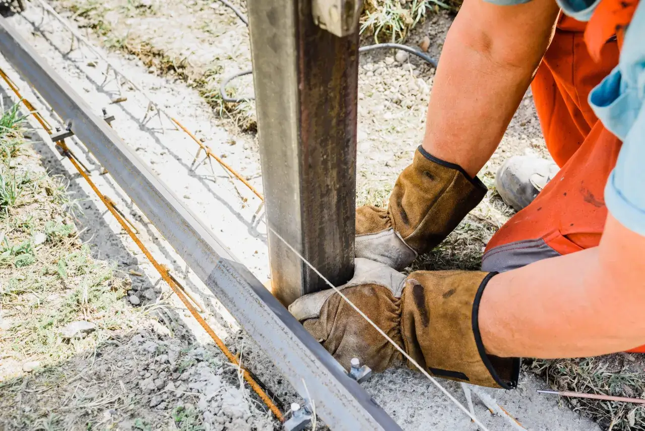 Pracownik w rękawicach montuje panele ogrodzeniowe, łącząc metalowe elementy.