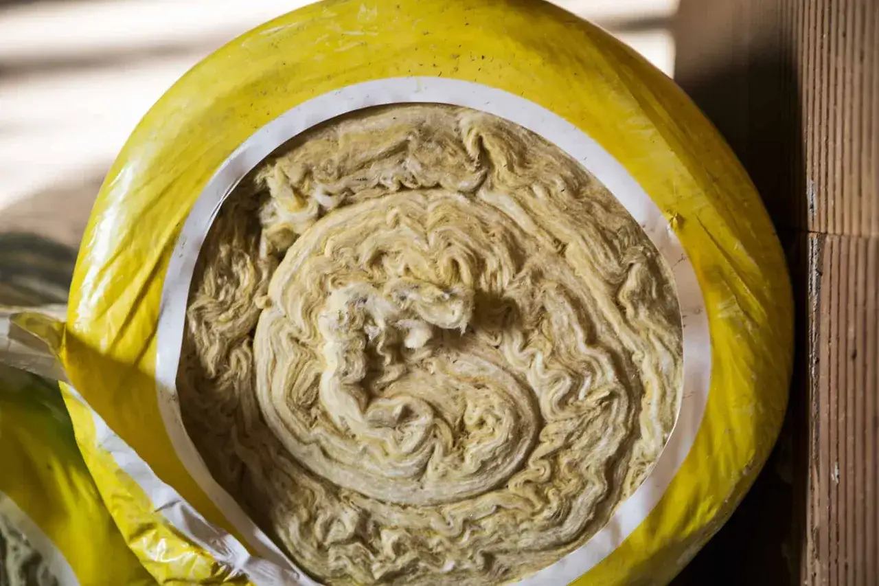 Zrolowana wełna skalna, materiał izolacyjny, w żółtej folii. Jej włóknista struktura przypomina naturalne minerały.