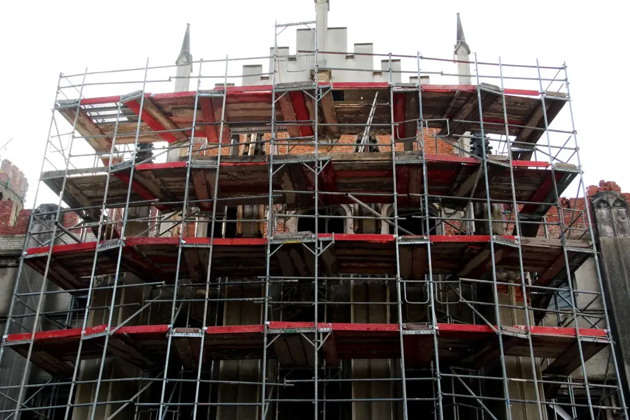Skomplikowane rusztowanie metalowe wokół zabytkowego budynku, pokazujące, jak zrobić rusztowanie drewniane, by zapewnić bezpieczeństwo pracownikom.