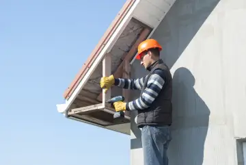 Budowlaniec w kasku montuje podbitkę z płyty OSB, używając wkrętarki.